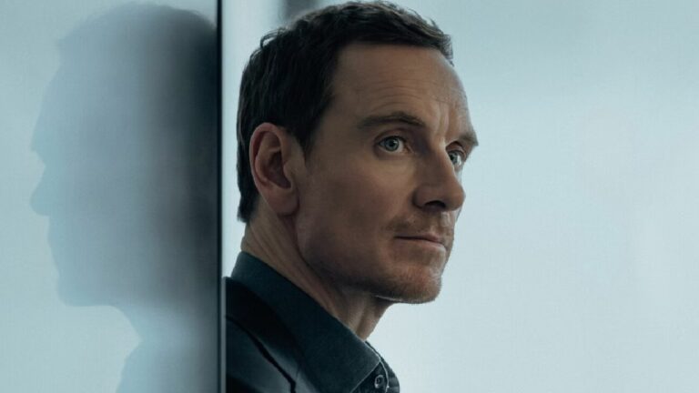 Michael Fassbender com expressão séria encostado em parede de vidro