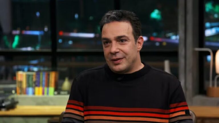 Marcelo Médici sentado em estúdio de programa de TV sorrindo durante entrevista