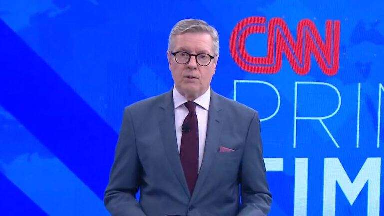 O jornalista Márcio Gomes, de terno azul e gravata bordô, apresenta o CNN Prime Time no estúdio do telejornal com fundo azul