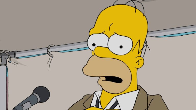 Cena da animação Os Simpsons, mostrando o personagem Homer Simpson com expressão preocupada diante de um microfone, em um ambiente interno iluminado