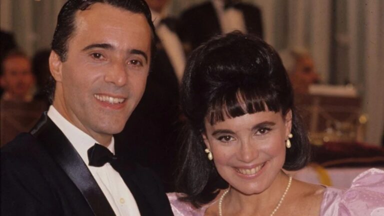 Casal vestido de forma elegante sorri em salão de festas durante cena da novela Rainha da Sucata da TV Globo