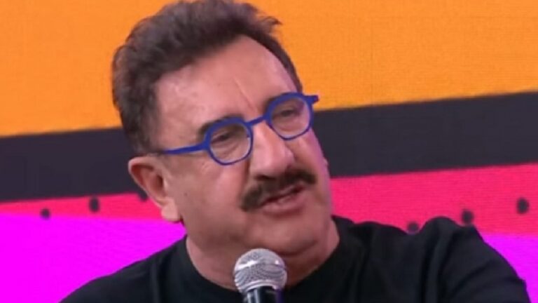 Ratinho segura microfone e fala durante participação em programa de TV com fundo colorido