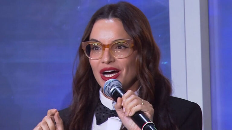 A chef Renata Vanzetto, com óculos e batom vermelho, fala ao microfone durante sua participação no evento Upfront 2026 da Globo