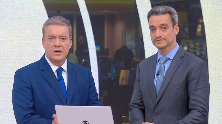 Roberto Kovalick de terno azul e Tiago Scheuer de terno cinza apresentam o telejornal Hora Um no estúdio da Globo