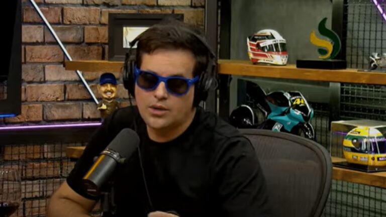 Rodrigo Scarpa usa óculos escuros e fones enquanto fala ao microfone durante gravação de podcast em estúdio