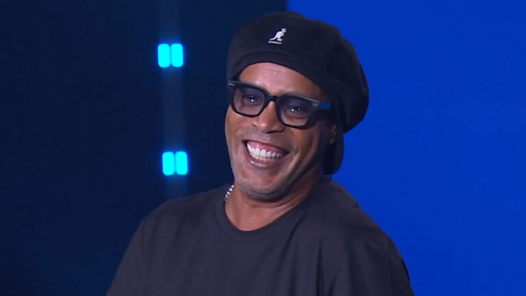 O ex-jogador Ronaldinho Gaúcho, com boina e óculos pretos, sorri no palco durante o evento Upfront 2026 promovido pela Globo