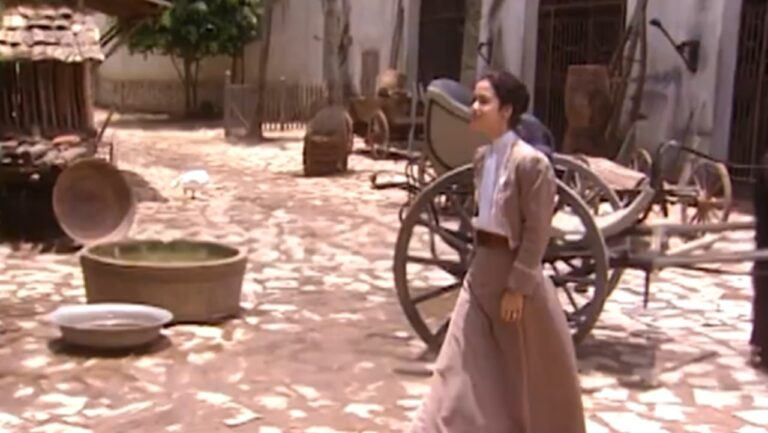 Angélica caminha pelo pátio da fazenda com roupas de época observando o local em cena da novela Terra Nostra da TV Globo