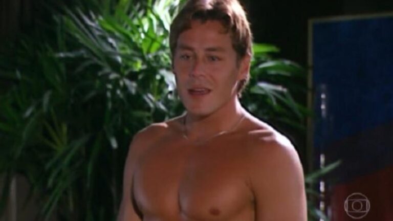 Homem sem camisa com expressão séria aparece em ambiente interno com plantas ao fundo em cena de novela da TV Globo