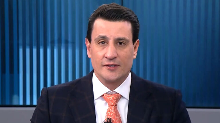 Tiago Pavinatto de terno e gravata laranja em enquadramento fechado no estúdio do programa Linha de Frente da Jovem Pan