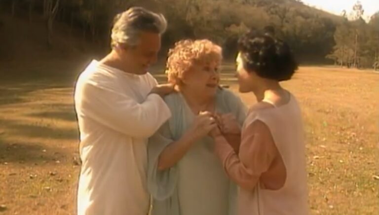 Cena da novela A Viagem mostra três personagens em um campo ensolarado, emocionados e sorrindo, simbolizando um reencontro espiritual em clima de paz e luz