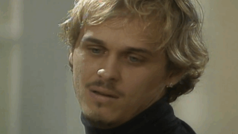 Cena da novela A Viagem mostra um homem de expressão melancólica e olhar distante, vestindo uma blusa preta de gola alta, em ambiente interno com iluminação suave