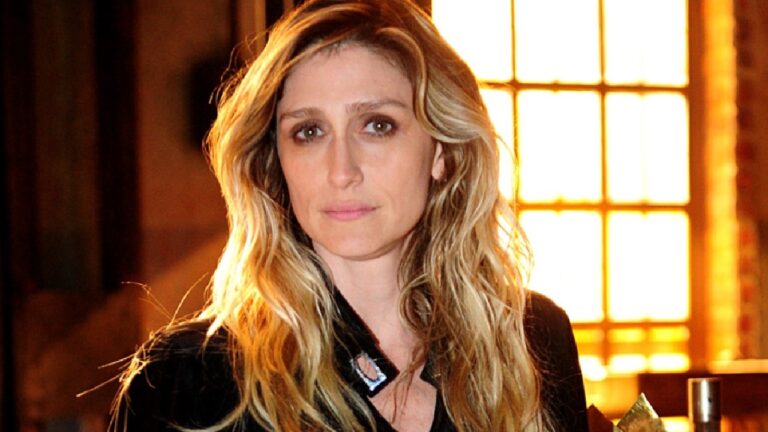 Amora Mautner com expressão séria posa em ambiente interno com iluminação quente e janela ao fundo