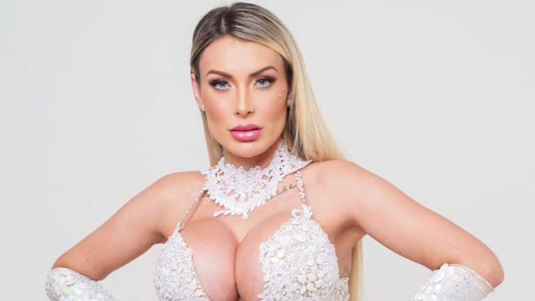 Andressa Urach com cabelos loiros e maquiagem destacada, vestindo um top branco de renda em um ensaio fotográfico