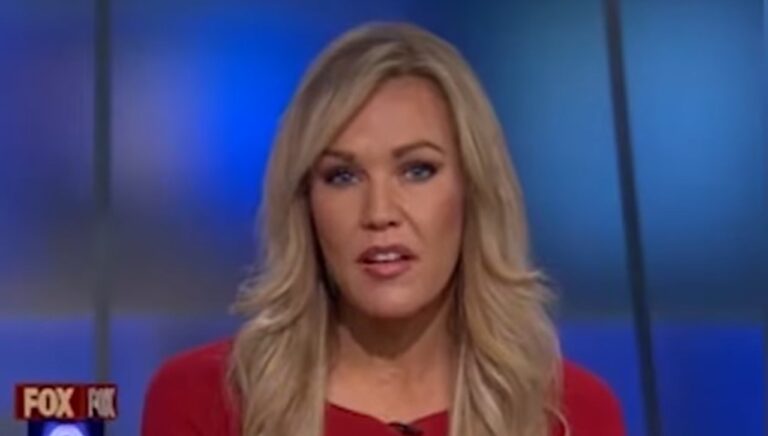 Mulher loira com blusa vermelha apresenta telejornal em estúdio com fundo azul