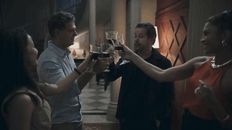 Quatro pessoas brindam com bebidas em uma cena escura