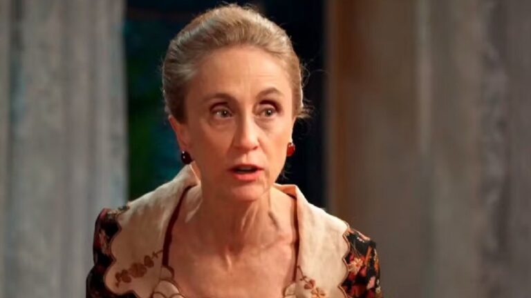 Mulher de cabelo preso e roupa de época fala com expressão séria em cena de novela de época