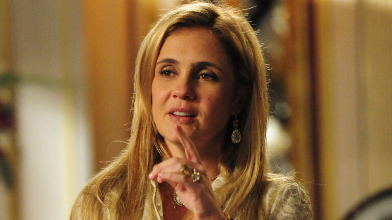 Adriana Esteves como Carminha com cabelo loiro, usando brincos e anéis grandes em cena da novela Avenida Brasil