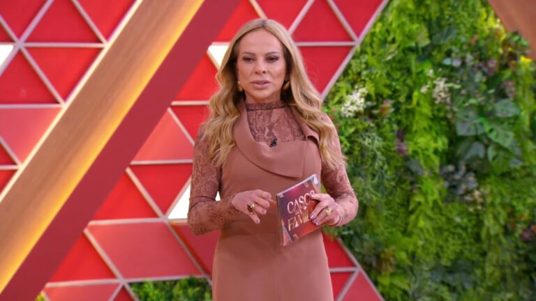 A imagem mostra Christina Rocha nos estúdios do SBT. Ela segura um cartão com o logotipo de Casos de Família, sugerindo que está em um cenário do SBT. O fundo é composto por painéis geométricos vermelhos e uma parede verde com plantas, transmitindo um visual moderno e colorido. A apresentadora veste roupa em tons terrosos e está com expressão séria, introduzindo um tema do programa