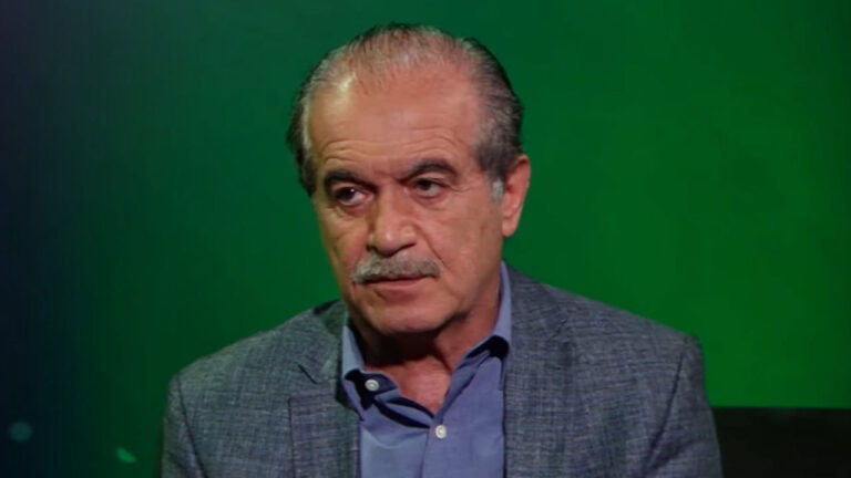 Chaim Zaher, empresário da educação, usando blazer cinza e camisa social azul com fundo verde em entrevista