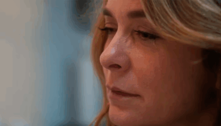 Close-up de uma mulher de expressão séria e olhar baixo, com semblante emocionado, possivelmente contendo as lágrimas. A iluminação suave destaca os traços do rosto, transmitindo um momento de introspecção ou tristeza