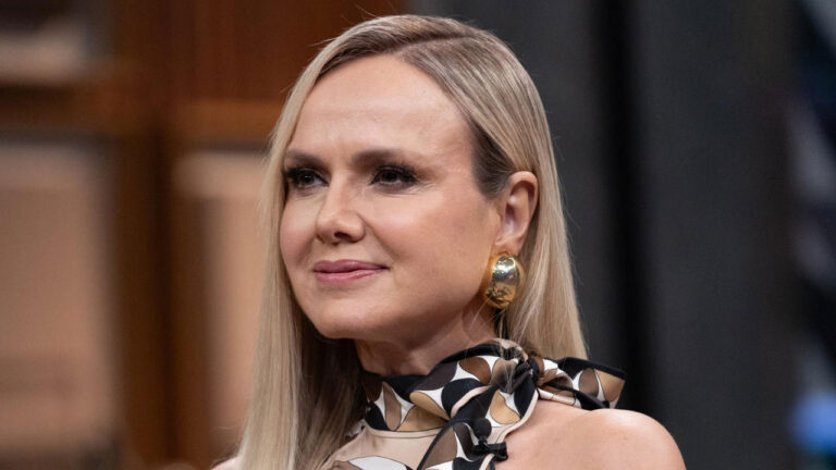 Apresentadora Eliana com cabelo loiro liso, usando um lenço com estampa geométrica e brinco grande dourado