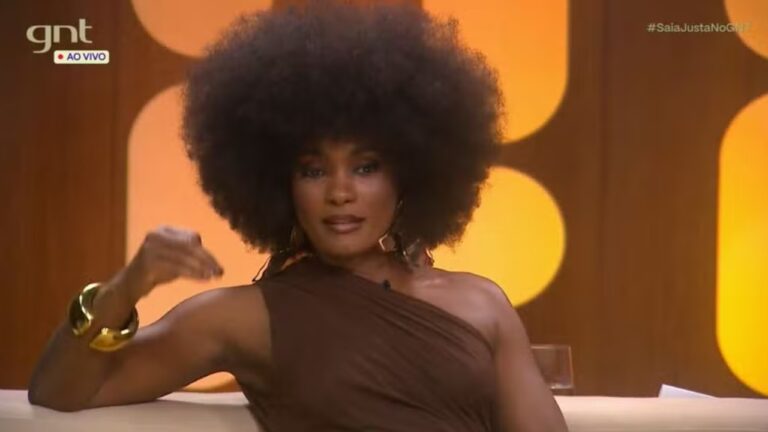 A imagem mostra uma mulher com cabelo afro volumoso, usando um vestido marrom de um ombro só e acessórios dourados