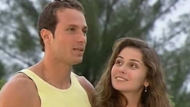 Homem e mulher conversam sorrindo ao ar livre, em cena ensolarada com árvores ao fundo