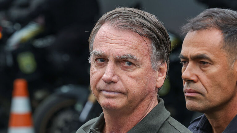 Ex-presidente Jair Bolsonaro em plano fechado, usando camisa polo verde-oliva, com um segurança ao seu lado