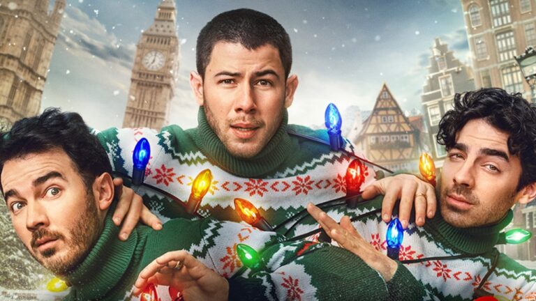 Três homens com suéteres natalinos e luzes coloridas posam juntos em cenário de inverno festivo