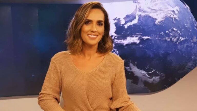 Mulher sorri diante de um painel que exibe imagem do planeta Terra vista do espaço, sugerindo um estúdio de telejornal ou programa de notícias