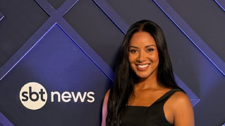 Mulher sorrindo de vestido preto em frente ao painel azul do SBT News iluminado por luz lateral