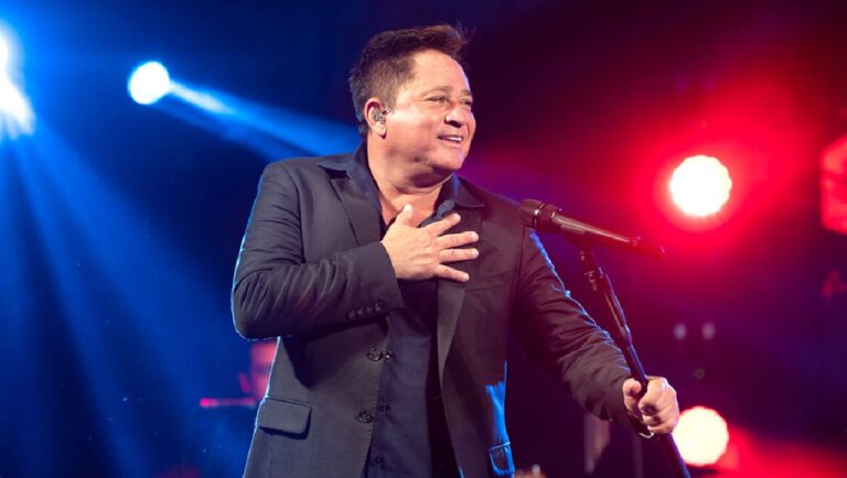 Cantor Leonardo se apresenta no palco, vestindo terno escuro e segurando o microfone enquanto sorri para o público, sob luzes coloridas de show