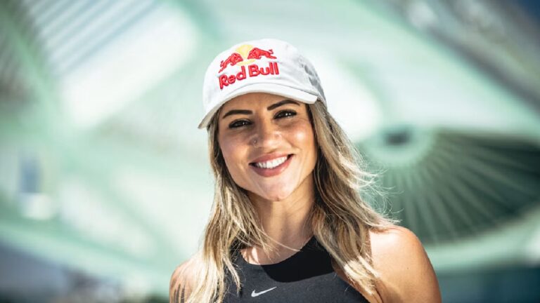A imagem mostra uma mulher sorridente ao ar livre, usando um boné branco com o logotipo da Red Bull e uma regata preta com o símbolo da Nike