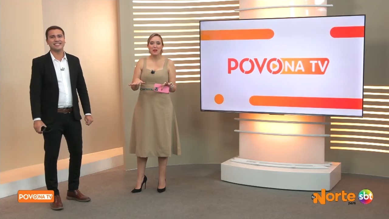 A imagem mostra dois apresentadores em um estúdio de TV durante o programa Povo na TV, exibido pela TV Norte Pará. O âncora Márcio Lins, de terno escuro e camisa branca, sorri para a câmera. Ao lado, Bianca Teixeira veste um vestido bege e segura um celular rosa. Atrás deles, uma tela exibe o logotipo do programa com tons de laranja e branco, e o cenário é iluminado com luzes quentes e painéis horizontais