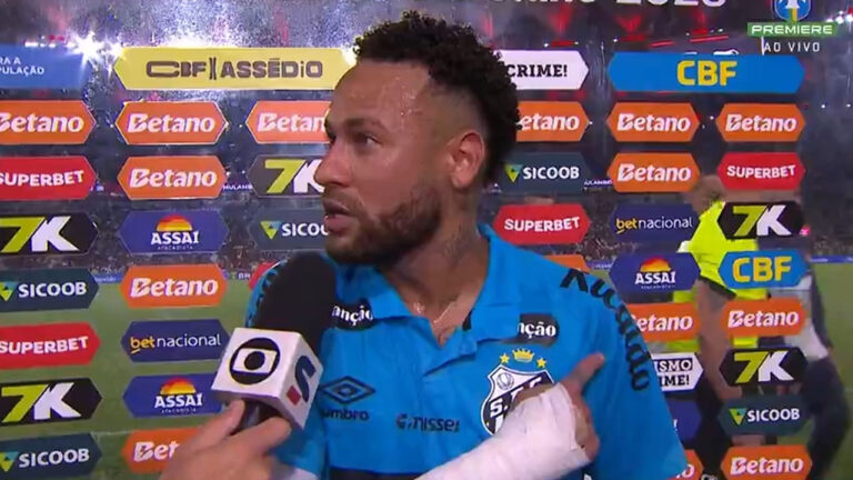 Jogador Neymar com a camisa do Santos dando entrevista após jogo com a mão enfaixada em frente a um painel de patrocinadores
