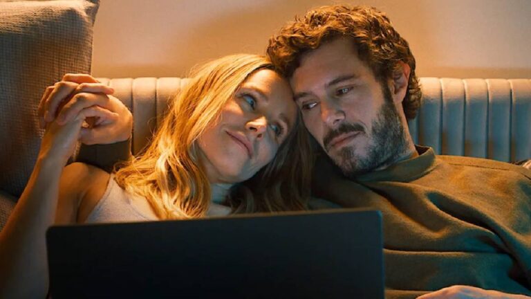 Casal deitado no sofá assiste algo em um laptop, trocando olhares carinhosos sob luz suave e ambiente acolhedor