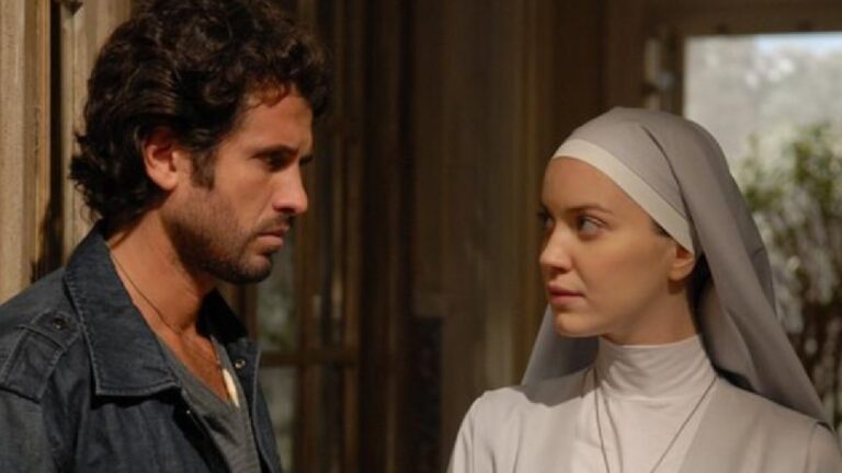 Homem encara mulher vestida de freira em cena dramática ambientada em local com iluminação suave e tons terrosos