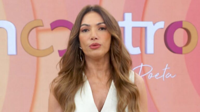 A imagem mostra uma apresentadora em um estúdio de televisão, posicionada diante de um painel colorido com o logotipo do programa “Encontro”. Ela veste uma blusa clara e usa o cabelo solto, com ondas leves. O fundo em tons de laranja e rosa reforça o estilo vibrante característico do cenário do programa matinal