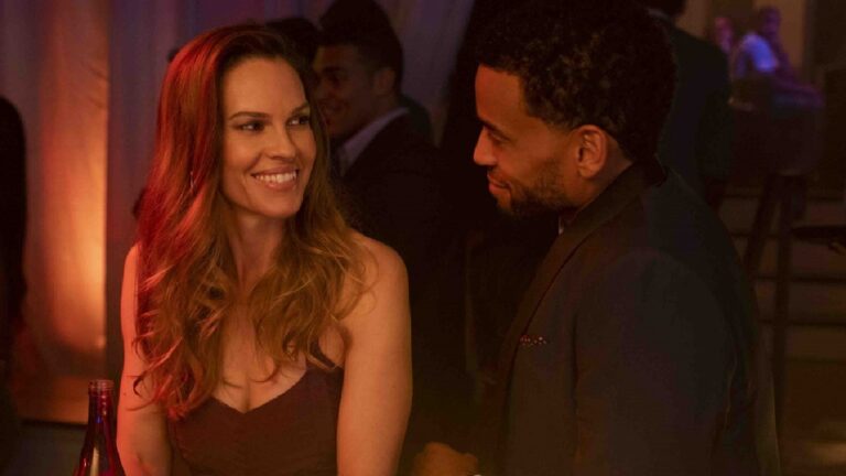 Mulher e homem trocam sorrisos em um bar com iluminação quente e ambiente intimista, sugerindo uma conversa descontraída ou cena romântica