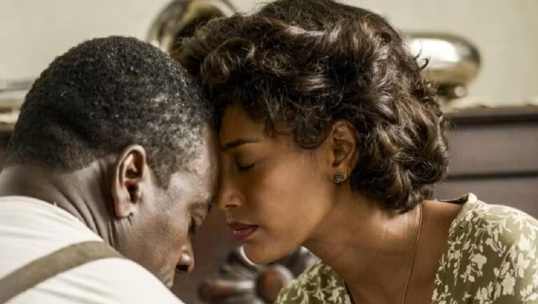 Casal em momento íntimo encosta as testas com olhos fechados, transmitindo consolo e conexão emocional em ambiente doméstico de época