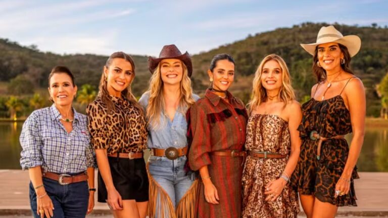 Grupo de mulheres com trajes country posa sorrindo ao ar livre com lago e montanhas ao fundo