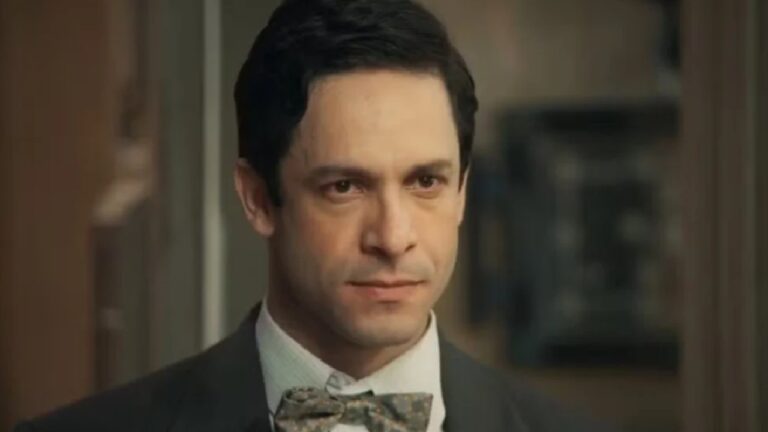 Homem de terno e gravata borboleta com expressão séria em ambiente interno