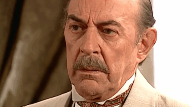 Homem idoso de expressão séria usa terno claro e gravata em cena de época ambientada em ambiente interno