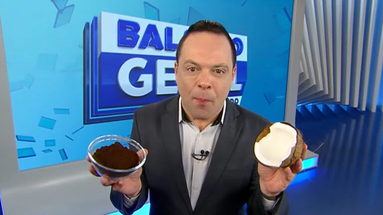 Thiago Gardinali, vestindo terno escuro, segura uma tigela com café em uma mão e meio coco na outra, em estúdio de telejornal com fundo azul e o logotipo do programa Balanço Geral ao fundo
