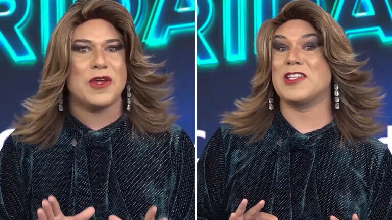 Tiago Barnabé caracterizado como Barnabela, com peruca loira, maquiagem forte e blusa de paetês verdes no palco