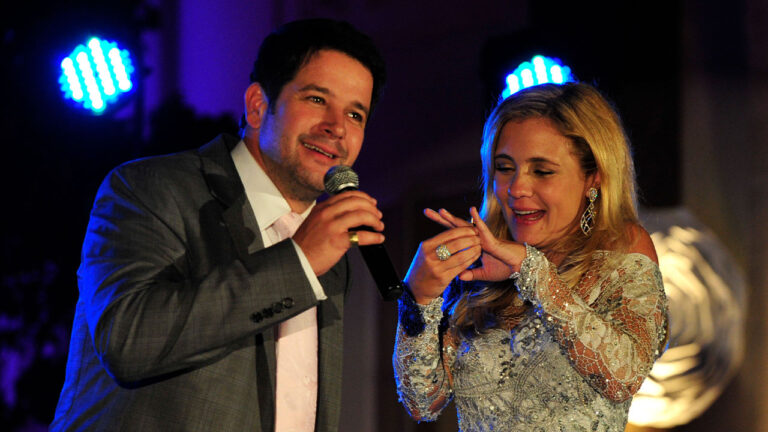 Murilo Benício (Tufão) e Adriana Esteves (Carminha) sorriem no palco em cena do aniversário de casamento dos personagens na novela Avenida Brasil