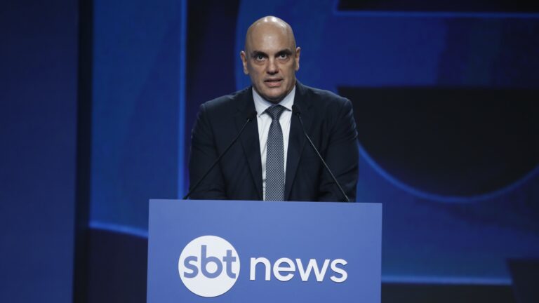 SEXTA: Alexandre de Moraes e Lula superam Aqui Agora e fazem audiência do SBT crescer XX% SÁBADO: Às 6h da manhã, reprise do Globo Rural tem mais público que Jornal da Record e SBT Brasil DOMINGO: Sem Roberto Cabrini, Domingo Espetacular despenca e marca pior ibope em XX semanas A imagem mostra Alexandre de Moraes, vestido de terno e gravata, falando em um púlpito azul com o logotipo SBT News. Ele está diante de dois microfones, em um cenário escuro com iluminação azul, típico de eventos jornalísticos ou debates promovidos pela emissora
