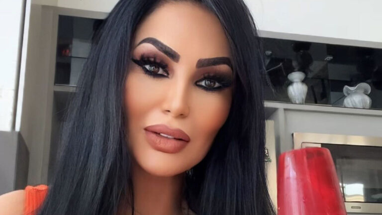 Ana Paula Oliveira com cabelo preto longo e maquiagem escura e marcante nos olhos posa para selfie segurando uma taça vermelha