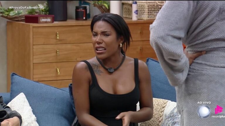 A imagem mostra Carol Lekker, participante do reality show A Fazenda, exibido pela Record, durante uma conversa dentro da casa. No canto superior esquerdo aparece a hashtag #ProvaDoFazendeiro, e no canto inferior direito o logotipo da emissora com o selo “ao vivo”. Ela está sentada em um sofá, discutindo, enquanto outra pessoa, de roupão cinza, está de pé ao seu lado