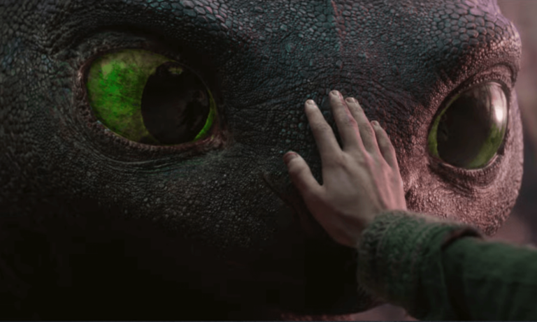 Close-up de um grande dragão de olhos verdes luminosos, com pele escura e textura rugosa, enquanto uma mão humana toca suavemente seu focinho em um gesto de confiança e conexão.